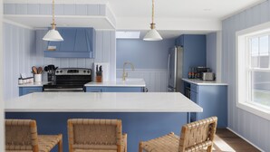 Una cocina con una isla central, armarios azules, encimeras blancas y sillas de mimbre.