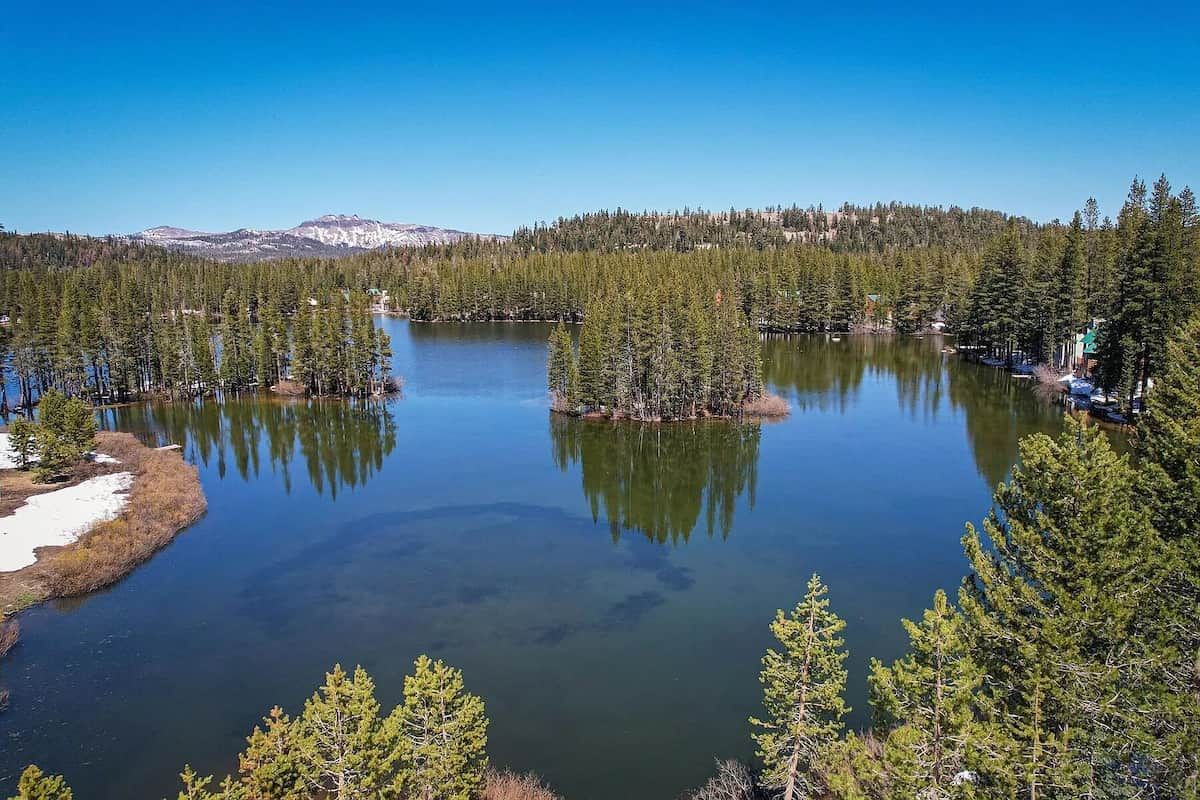 Un lac entouré d’une forêt dense, avec une chaîne de montagnes en arrière-plan.