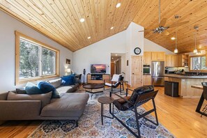 Un vaste espace de vie doté d’un haut plafond, d’un plancher en bois, d’un grand canapé, d’une table basse et d’un téléviseur.