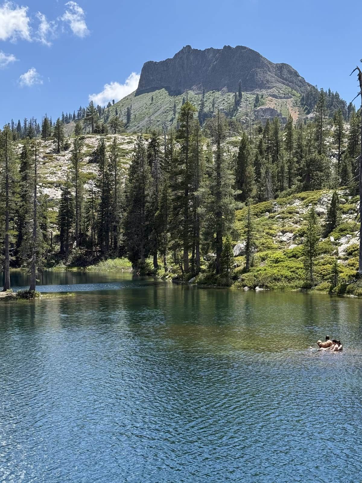 A mountain landscape with a clear lake and a person swimming.