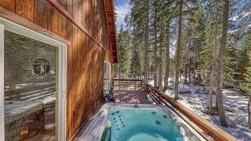 A wooden cabin with a hot tub and a deck overlooking a forest.