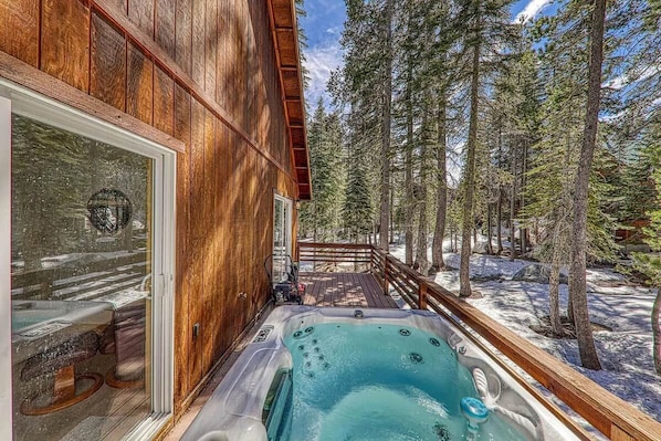 Une cabane en bois dotée d’un bain à remous et d’une terrasse offrant une vue sur une forêt.