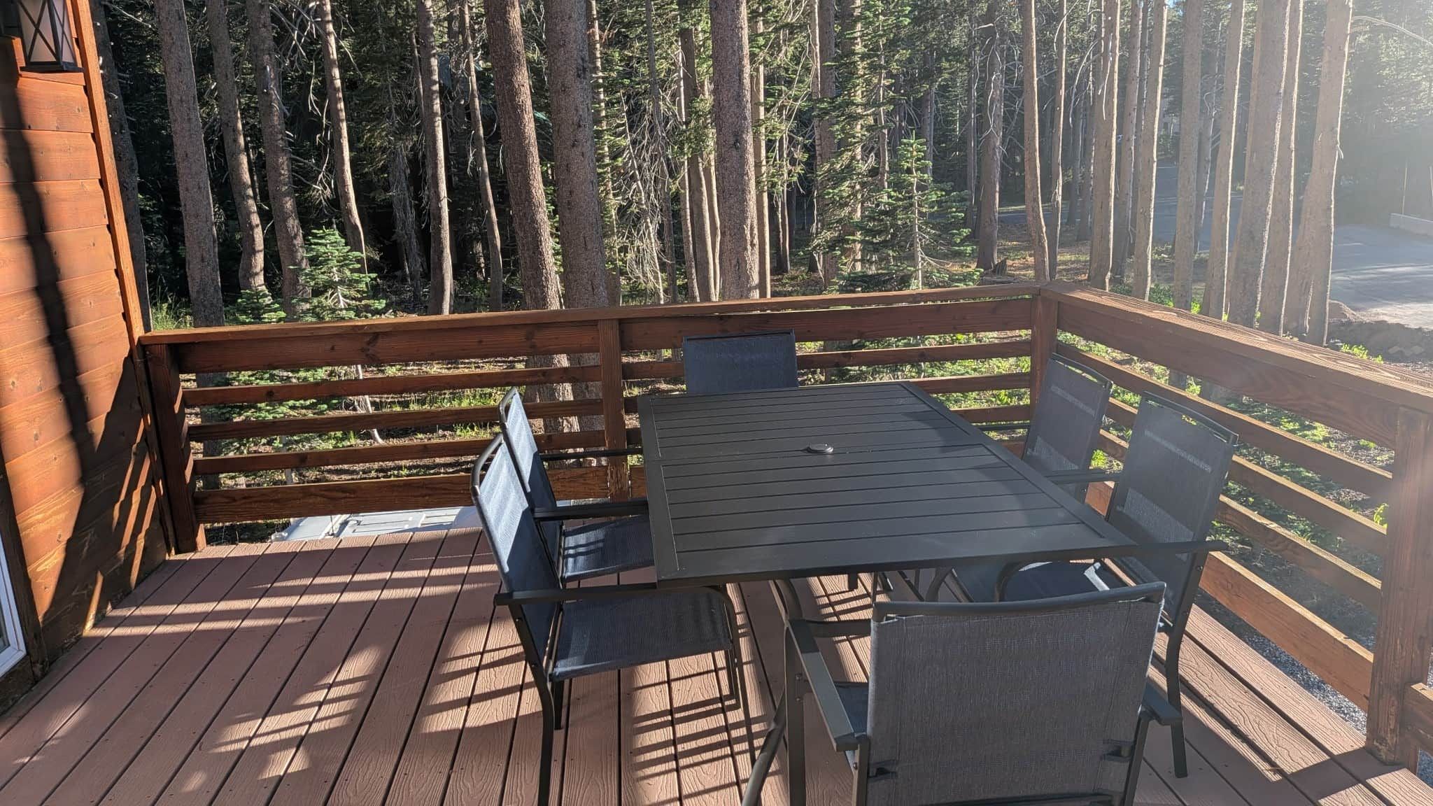 A wooden deck with a table and chairs, surrounded by tall trees.