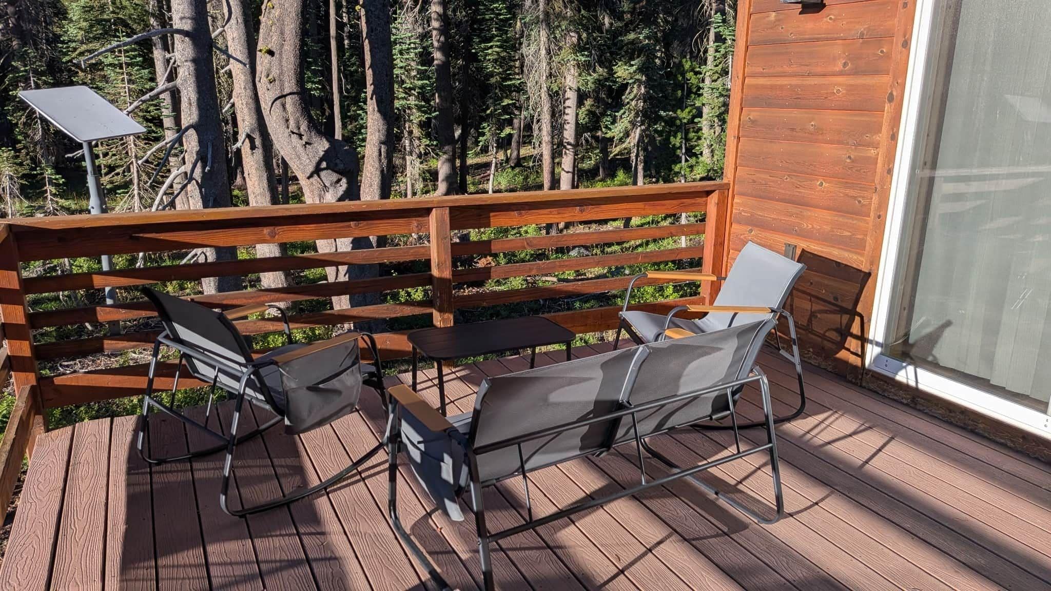 A wooden deck with a table and chairs, surrounded by a wooden railing, overlooking a forest.
