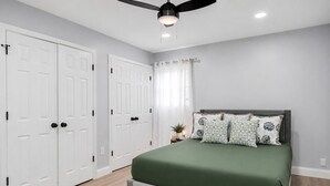 Une chambre à coucher avec un lit, un ventilateur de plafond, une porte double blanche et une fenêtre avec des rideaux.