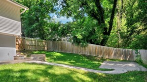 Un jardin avec une clôture en bois, un chemin en béton et une pelouse verdoyante.