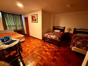 Habitación de hotel con dos camas, un escritorio con una computadora portátil, piso de parqué de madera y un cuadro en la pared.