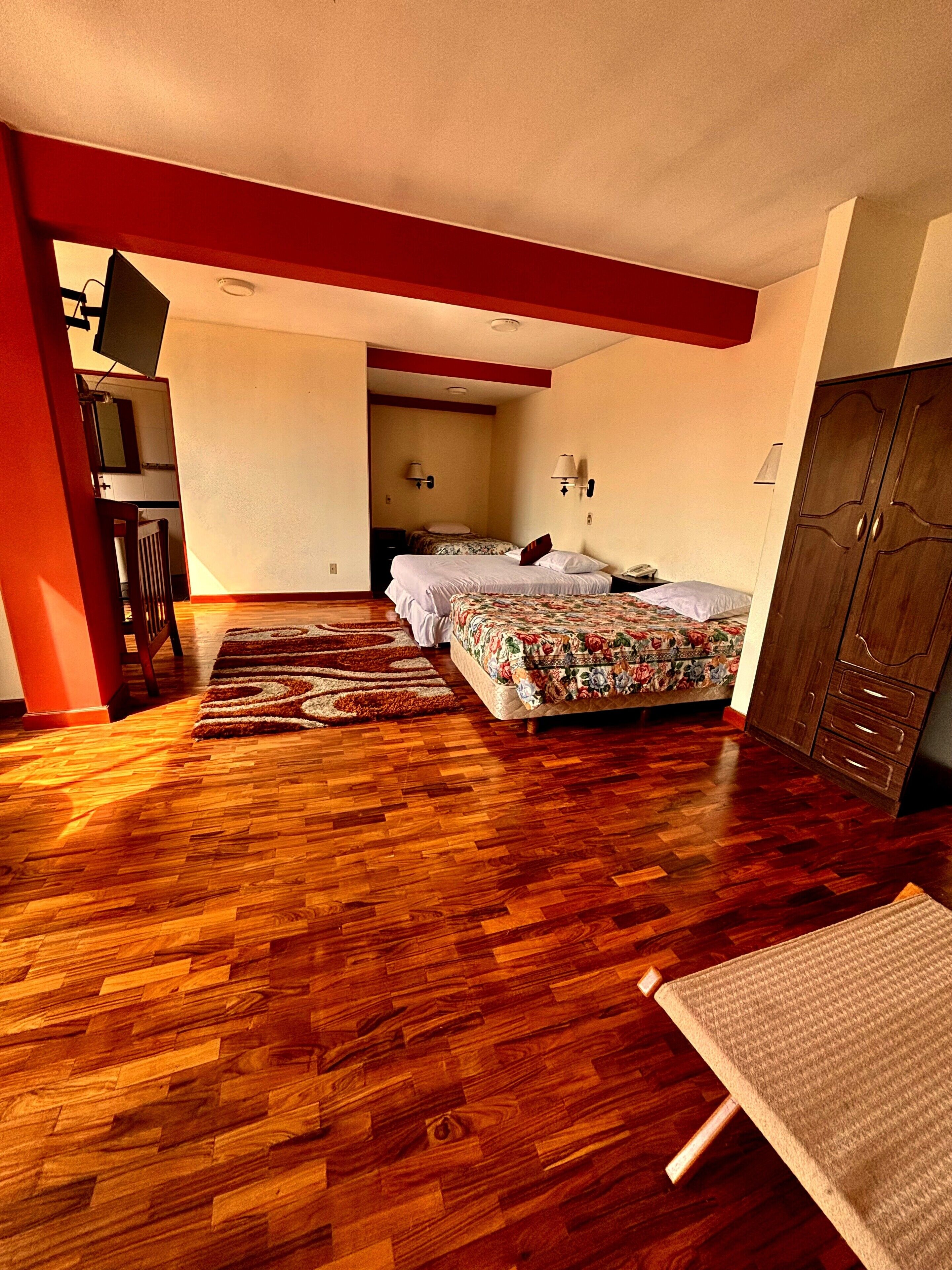 Quarto com piso de madeira, cama com roupa de cama floral, guarda-roupa e escrivaninha com luminária.