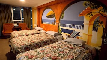Habitación de hotel con dos camas, una silla, una mesa y vista al mar a través de un ventanal arqueado.