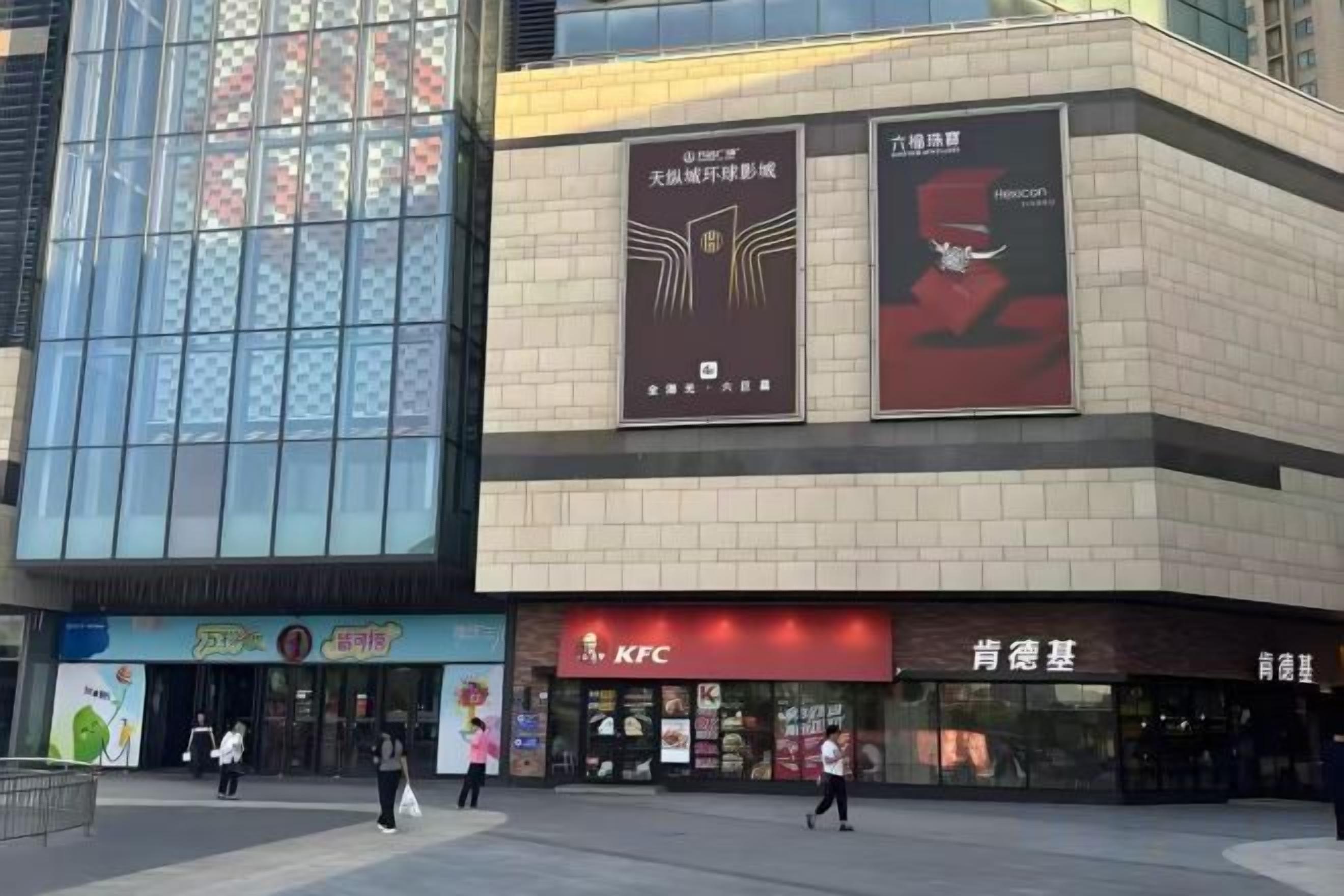 A commercial building with a glass facade, KFC, and other retail stores.