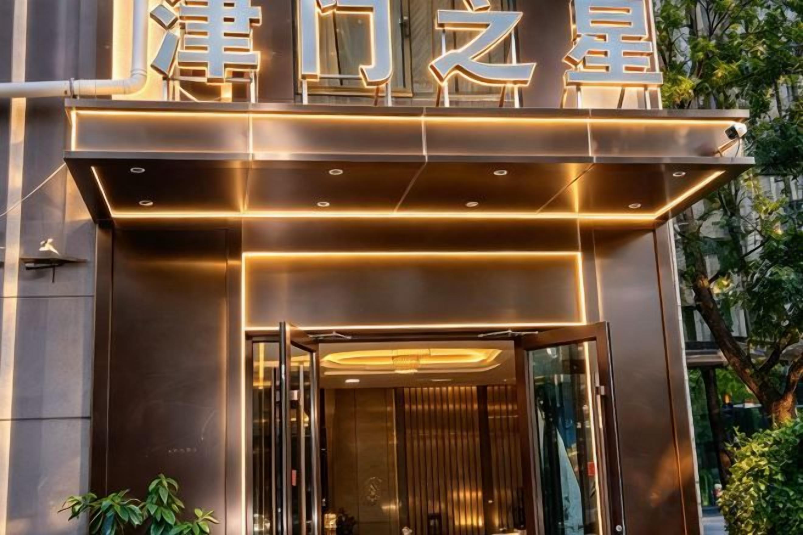 A hotel entrance with a modern design, featuring illuminated signage and a glass door.