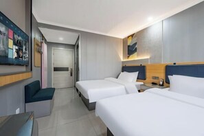 Habitación de hotel con dos camas, un escritorio, una silla y un televisor montado en la pared.