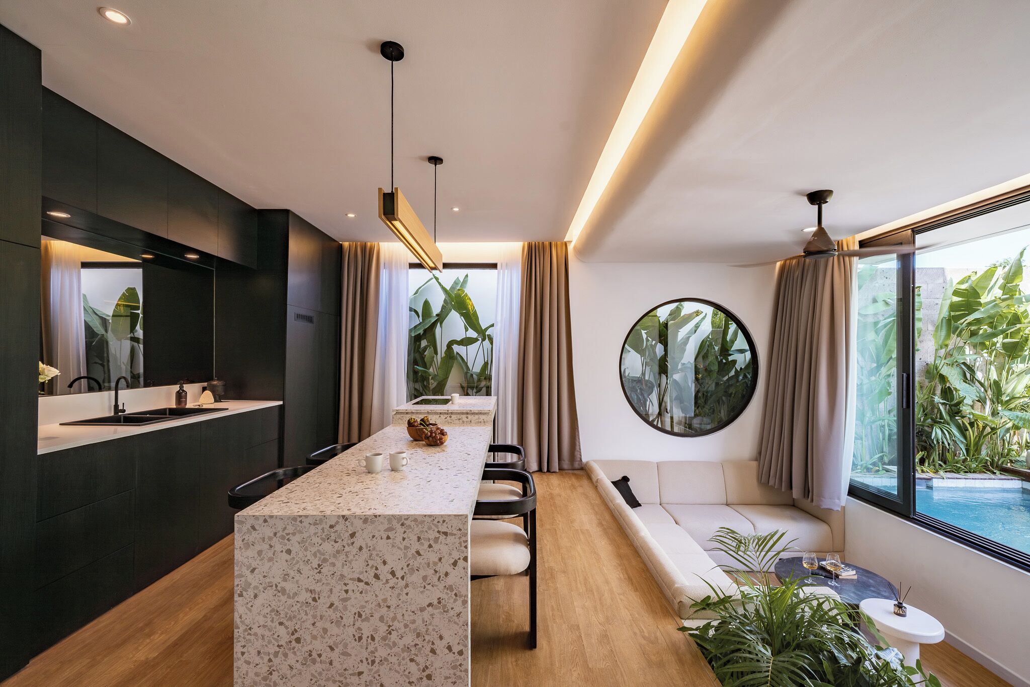 Una cocina moderna con una isla central, un área de comedor con una mesa redonda y un rincón de estar con vista a una piscina.