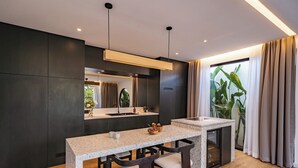 A modern kitchen with dark cabinetry, a granite countertop, and a built-in dishwasher. - Club Suma Villa 5 Bingin (Pecatu)