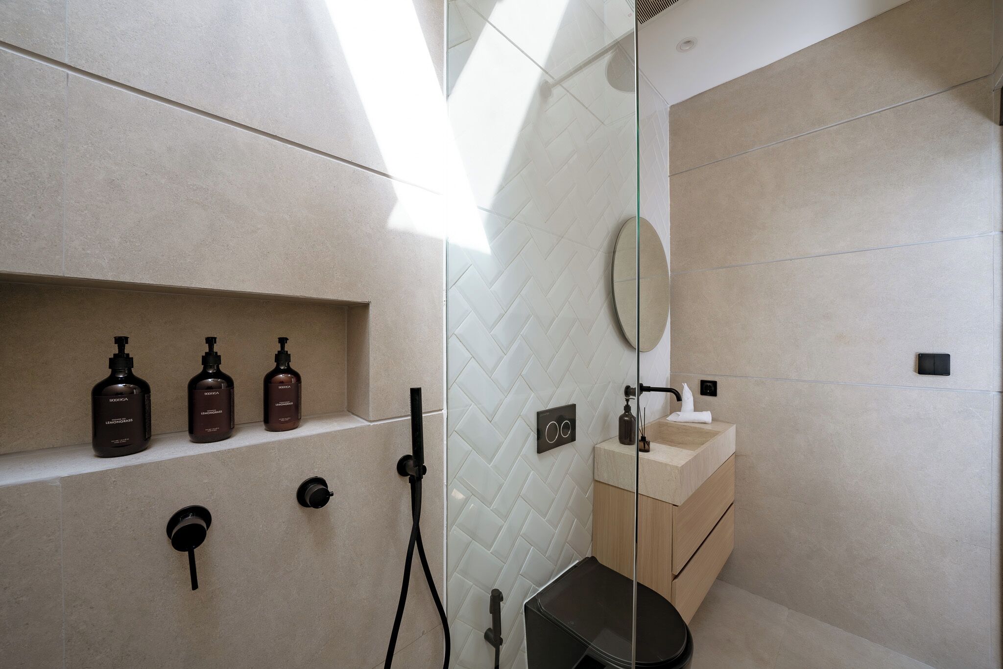 A modern bathroom with a herringbone tile pattern, a glass shower enclosure, and a wooden vanity.