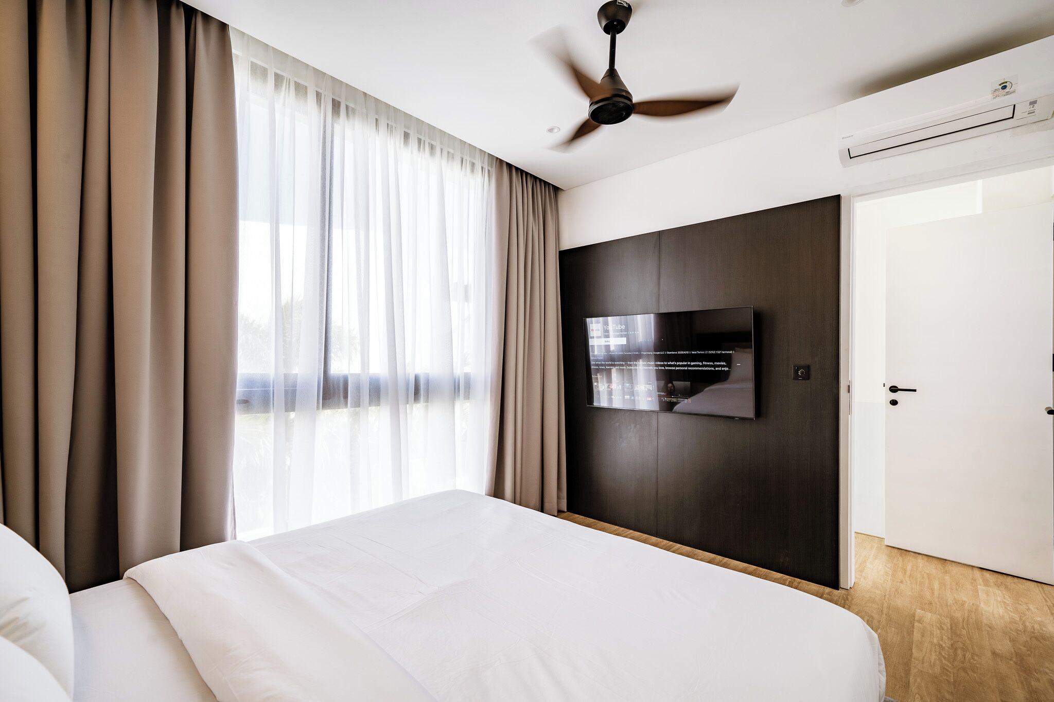 A hotel room with a bed, a ceiling fan, a TV mounted on the wall, and a door.