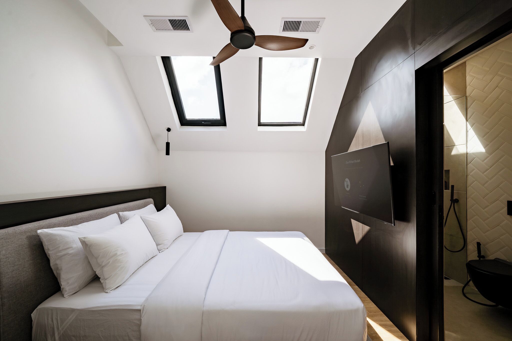Quarto moderno com cama, ventilador de teto, TV fixada na parede e claraboias.