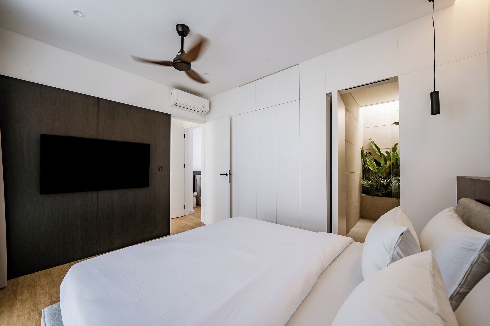 A modern bedroom with a large bed, a ceiling fan, a flat-screen TV, and a walk-in closet.