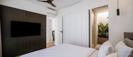 A modern bedroom with a large bed, a ceiling fan, a flat-screen TV, and a walk-in closet.