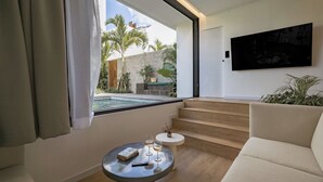 A modern living room with a pool view, a flat-screen TV, and a staircase leading to an outdoor area. - Club Suma Villa 5 Bingin (Pecatu)