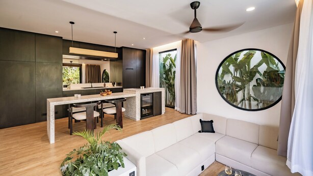 A modern kitchen with a dining area, a round mirror, and a living room with a sofa. - Club Suma Villa 5 Bingin (Pecatu)