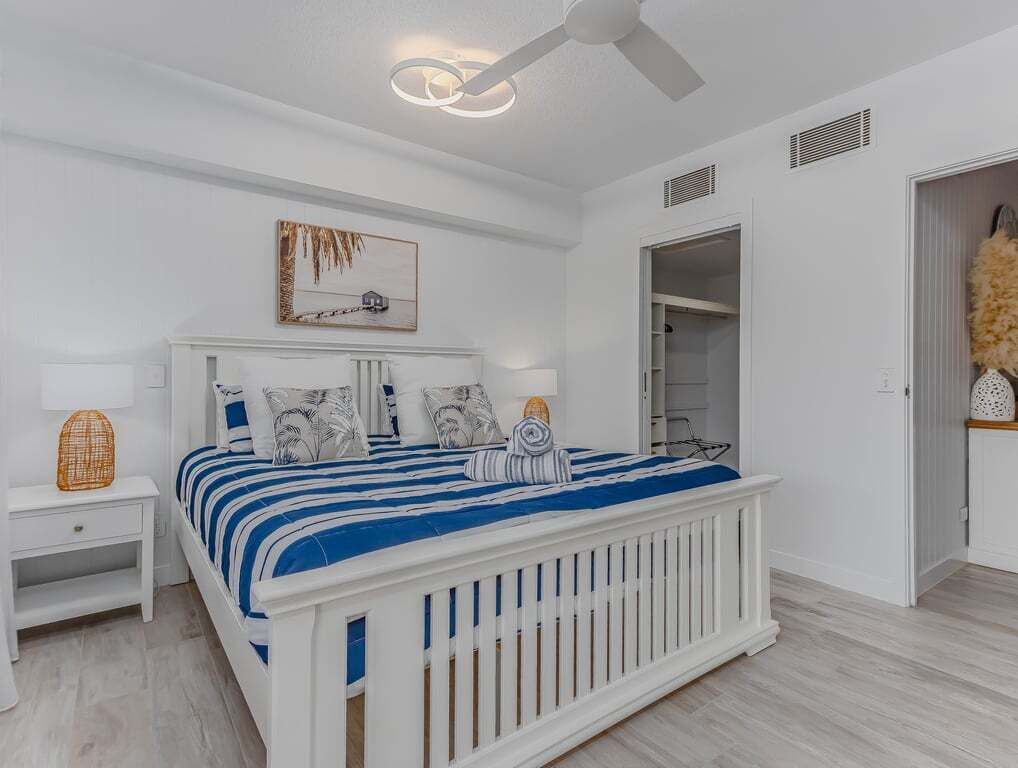 Ein Schlafzimmer mit einem weißen Bett, einem Deckenventilator, einem Nachttisch und einem Kleiderschrank.