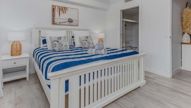 Een slaapkamer met een wit bed, een plafondventilator, een nachtkastje en een kledingkast.