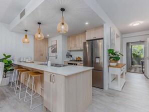 A modern kitchen with a large island, bar stools, stainless steel appliances, and pendant lighting. - Forever Summer at Drift North (Tweed)