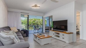Een moderne woonkamer met een bank, salontafel, tv-meubel en een balkon met buitenmeubilair.