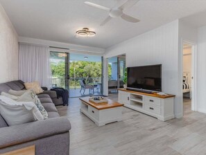 A modern living room with a sofa, coffee table, TV stand, and a balcony with outdoor furniture. - Forever Summer at Drift North (Tweed)