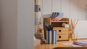 Een houten bureau met een gestreepte pennenhouder, een kleine plant en een lamp.