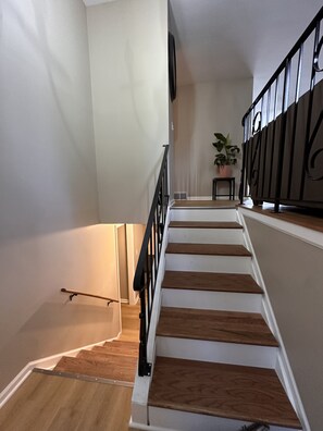 Eine Treppe mit Holzboden und einem schwarzen Geländer, die zu einer Zwischenebene mit einem Blumentopf führt.