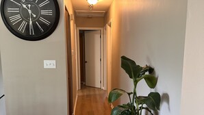 A hallway with a wall-mounted clock, a potted plant, and a door at the end.