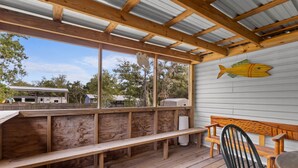 En overdækket terrasse med træbænke og et bord, med udsigt over et boligområde.