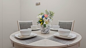 Et spisebord med hvide skåle og tallerkener, en marmorvase med blomster, og grå polstrede stole.