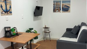 Een moderne woonruimte met een houten eettafel, een bank, een koffiezetapparaat en een aan de muur bevestigde televisie.