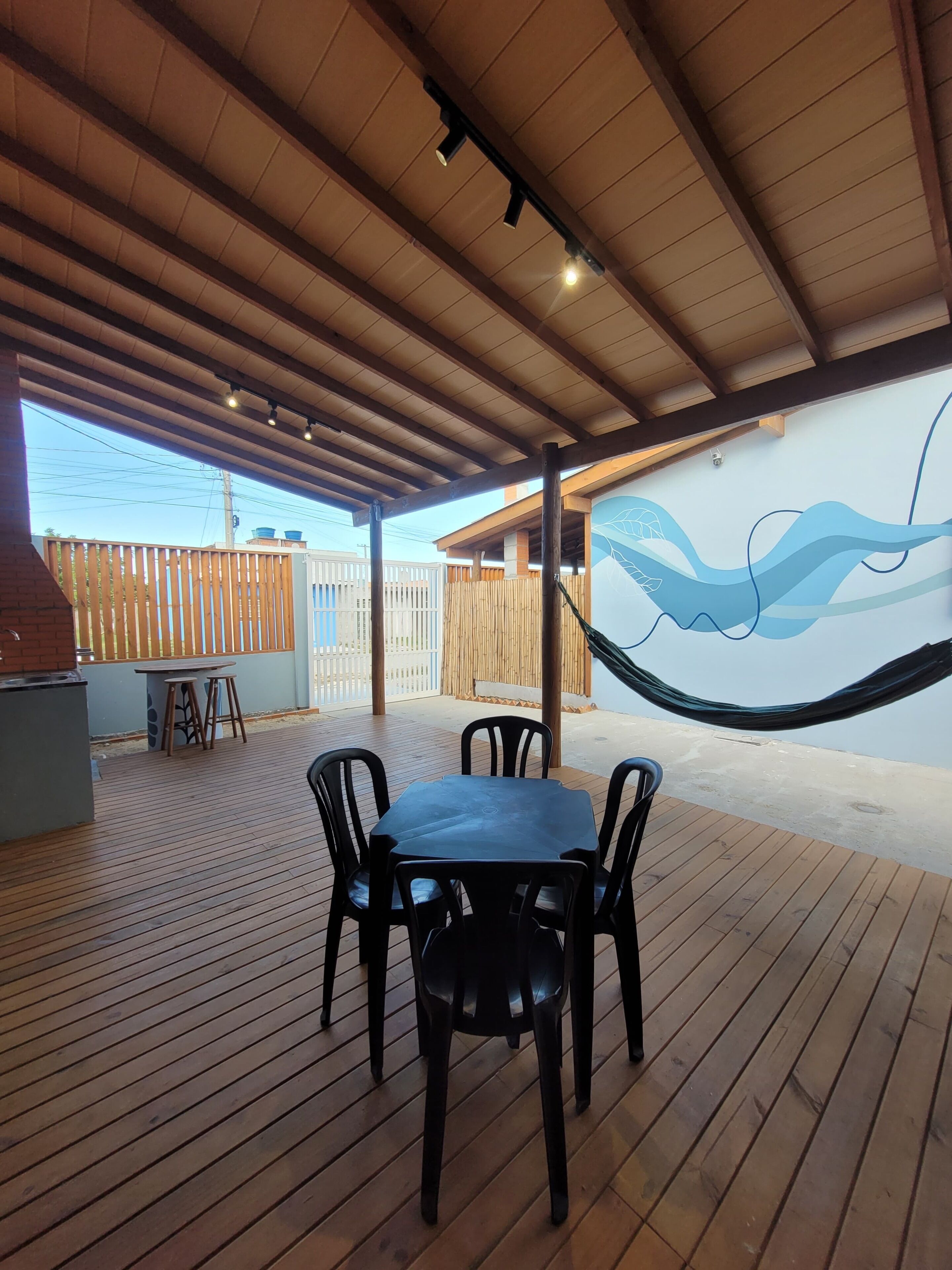 Un patio exterior con mesa y sillas de madera, una hamaca y una pared con diseño de olas.