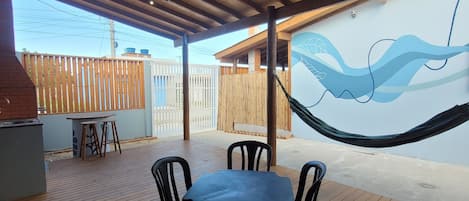 An outdoor patio with a wooden table and chairs, a hammock, and a wall with a wave design.