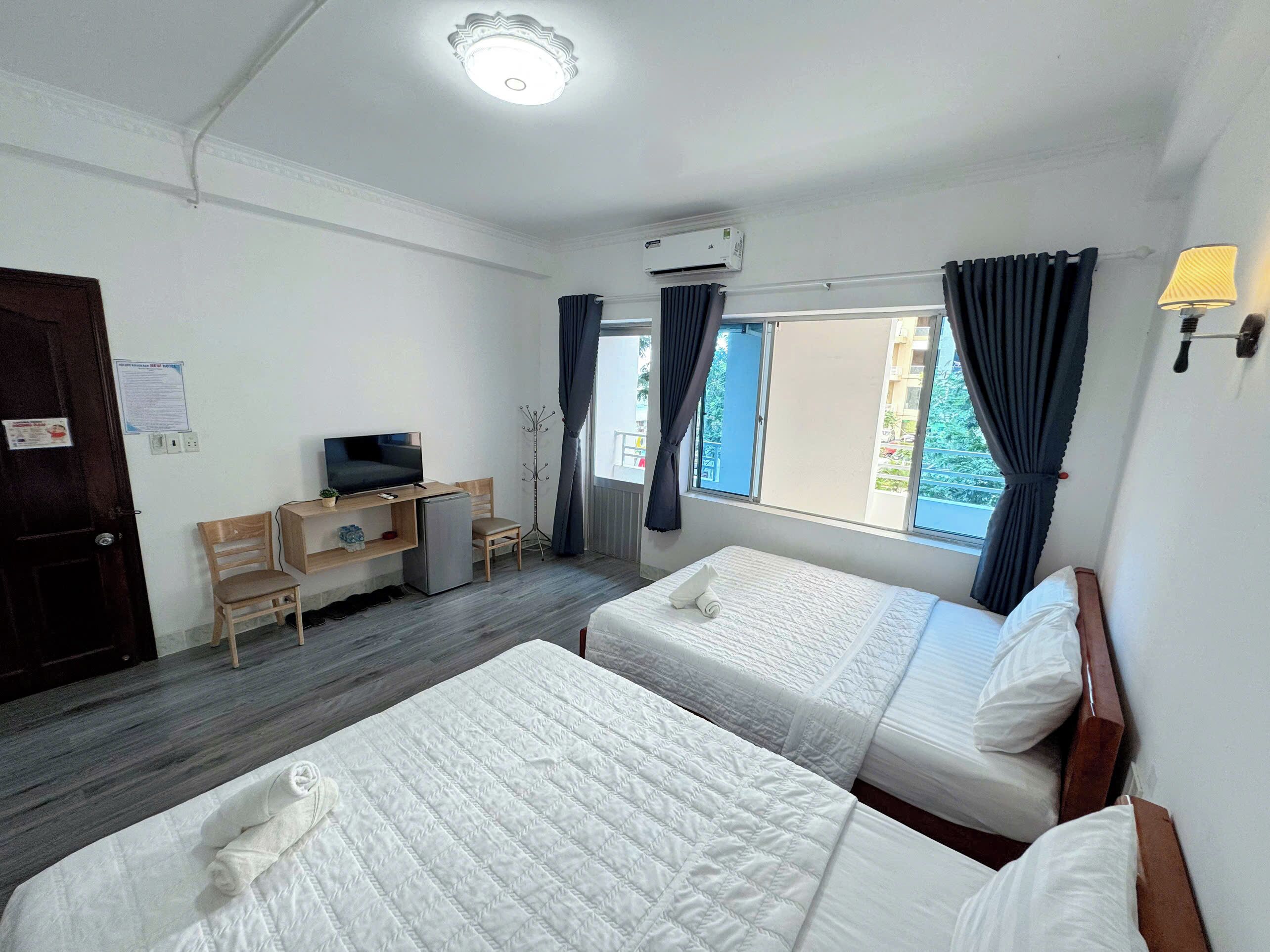 A hotel room with two beds, a desk with a television, a coat rack, and a window with curtains.