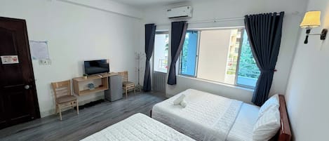 Habitación de hotel con dos camas, un escritorio con televisor, perchero y ventana con cortinas.