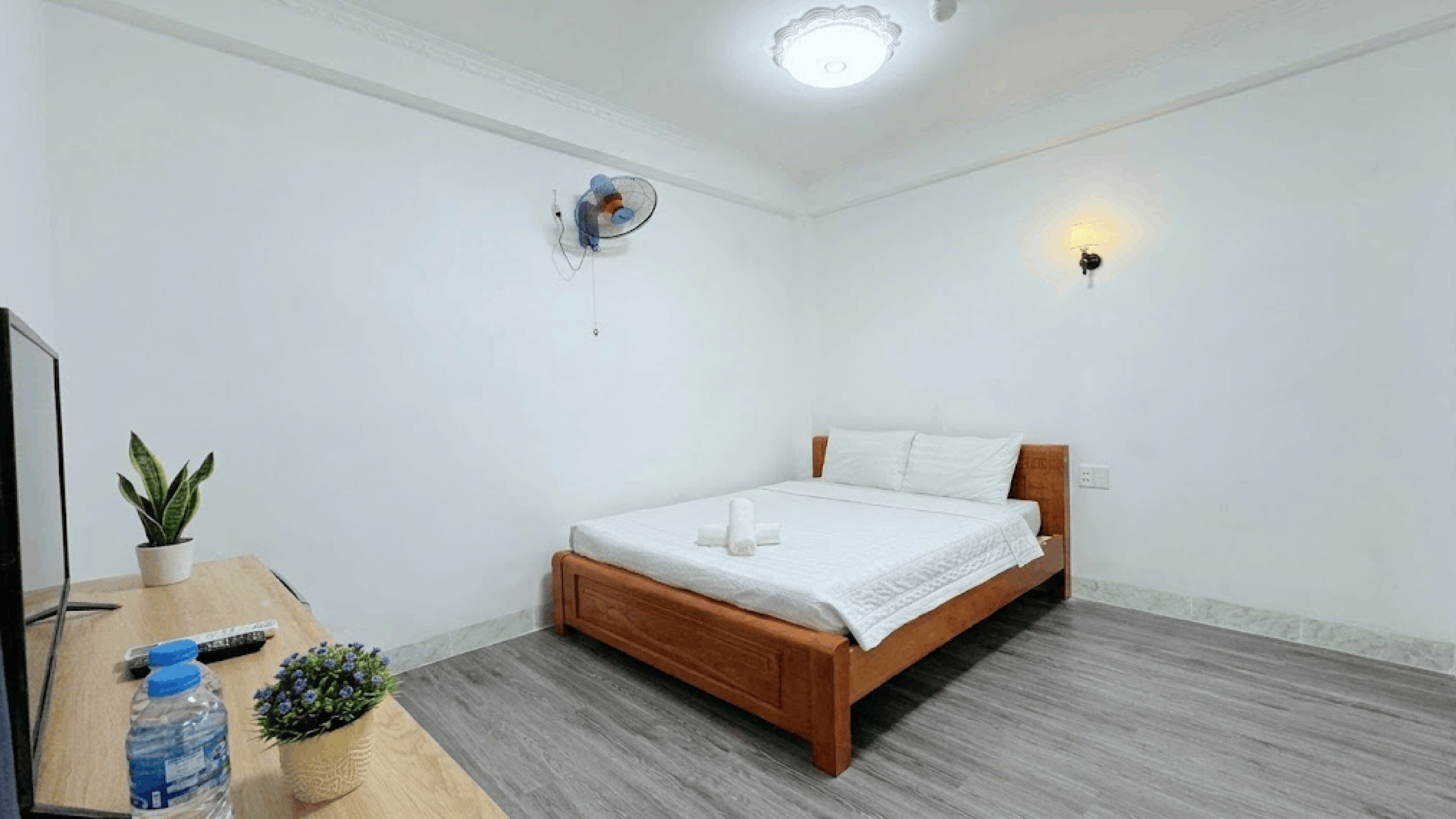 Un dormitorio con una cama de madera, un escritorio con una planta, una botella de agua y un control remoto.