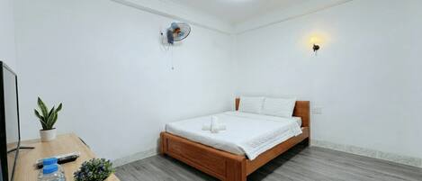Un dormitorio con una cama de madera, un escritorio con una planta, una botella de agua y un control remoto.