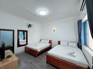 Ein Hotelzimmer mit zwei Einzelbetten, einem Schreibtisch mit Computer, einem Spiegel, einem Deckenventilator und einem Fenster mit Vorhängen.