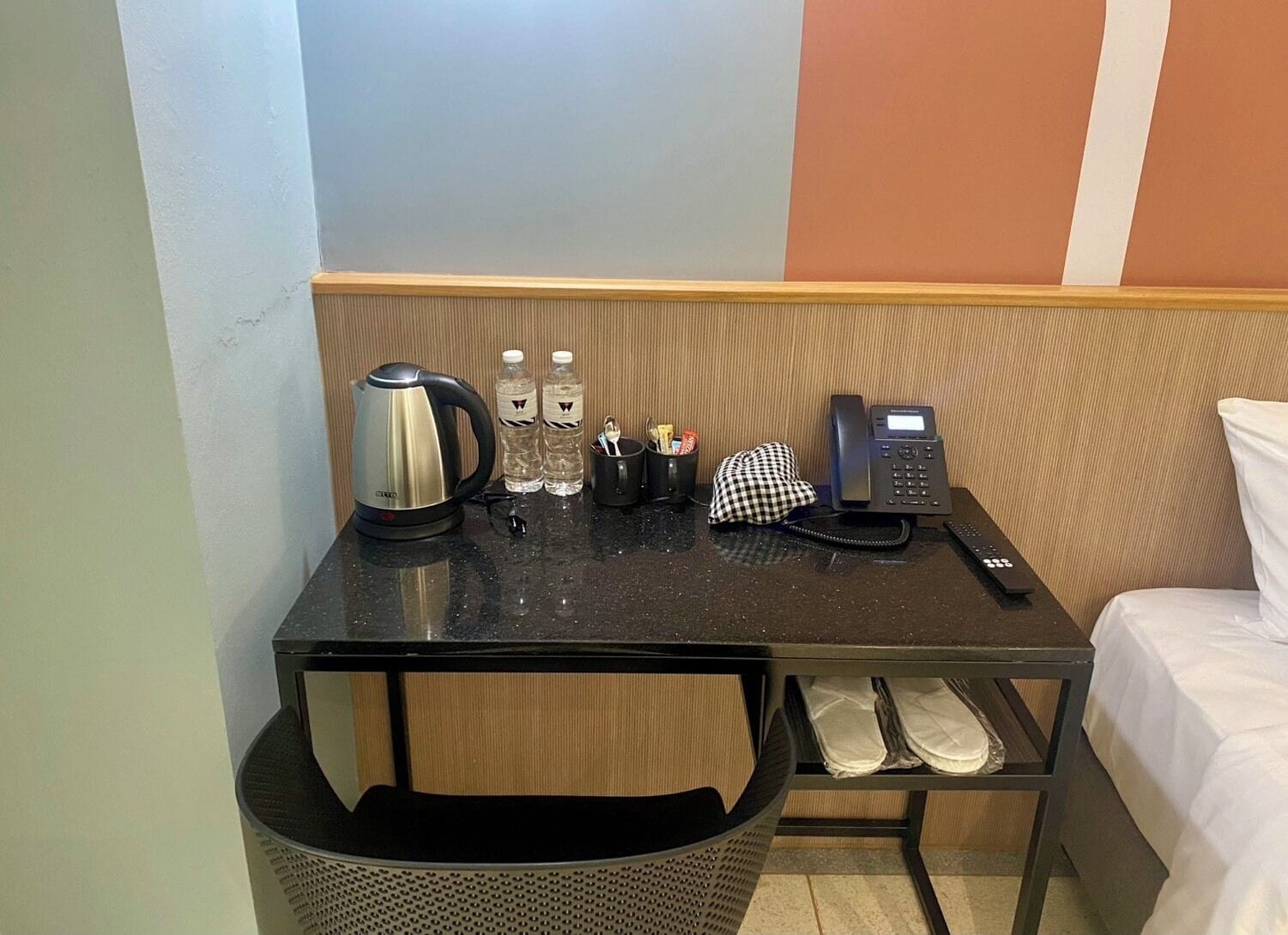 Hotelkamer met een tafeltje, een waterkoker, twee waterflesjes, een telefoon en een geruit kleed.