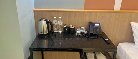 Habitación de hotel con una mesita, una tetera, dos botellas de agua, un teléfono y un mantel a cuadros.