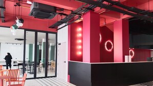 A modern interior with a red accent wall, a reception desk with circular light fixtures, and a patterned floor. - Witz Pop Ratchada (Bangkok)