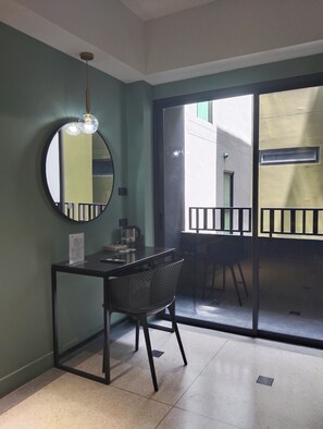 Habitació amb una taula, una cadira i un mirall gran. Hi ha una porta corredissa de vidre que dona a una zona exterior.