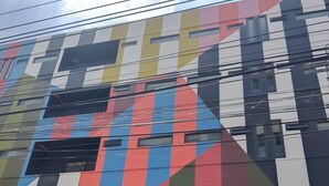 A multi-story building with a colorful facade, large windows, and visible power lines. - Witz Pop Ratchada (Bangkok)