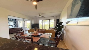 A spacious living area with a ceiling fan, a dining table with chairs, a sofa, and a television.
