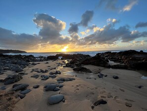 Una playa rocosa con huellas visibles y una puesta de sol al fondo.